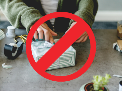 In the background, a person is wrapping a gift; there are supplies like paper, tape and scissors on their work surface. An overlay of a large red circle with a line through it indicates that this is to be avoided.